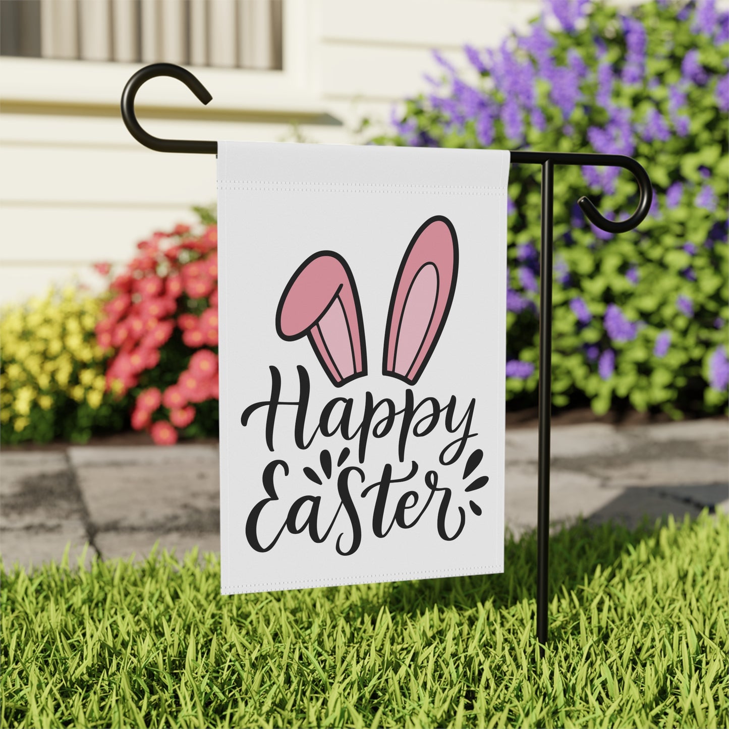 Garden flag with 'Happy Easter' and bunny ears design on a stand in front of flowers.