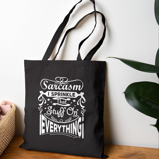 Black tote bag with white text on a wooden surface with a plant in the background